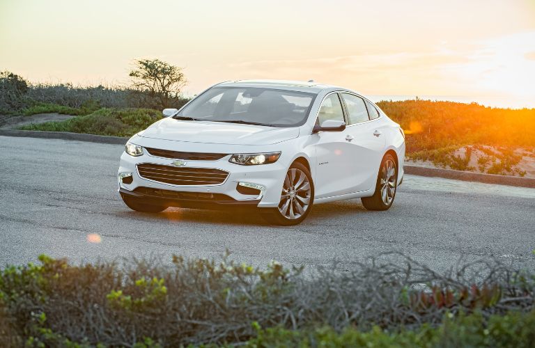 side view of white 2018 chevrolet malibu in front of grass and ocean
