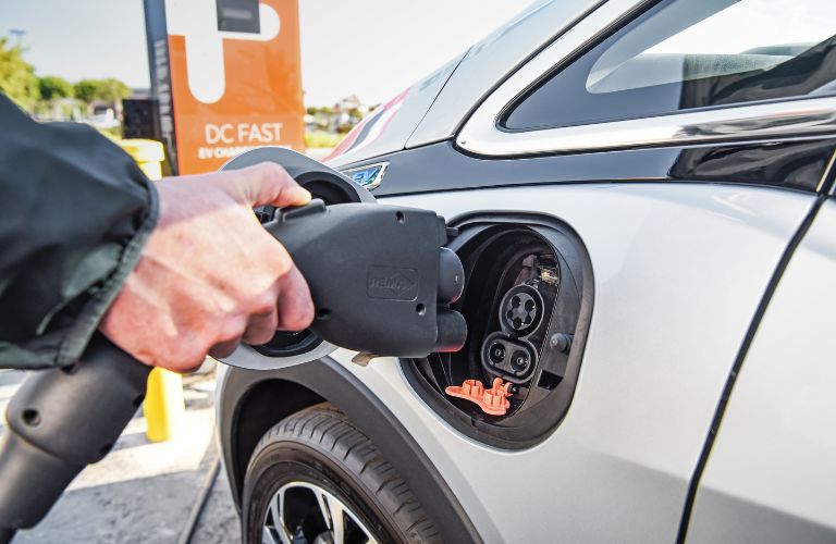 man using public charging station to charge silver 2019 chevrolet bolt ev