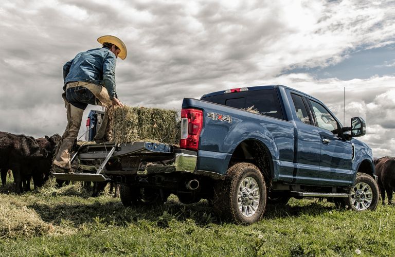 rear and side view of blue 2019 ford super duty as man loads bails of hay into bed