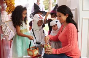 Woman giving chocolates to children playing trick and treat