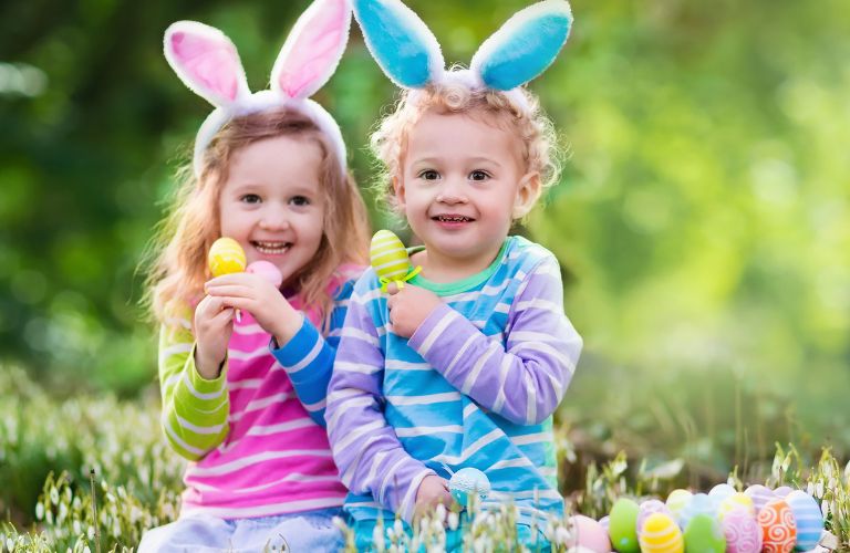 Two Smiling Kids with Bunny Ears on and Easter Eggs